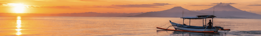 Traditional outrigger fishing boat on calm water at sunset with volcanoes on the horizon